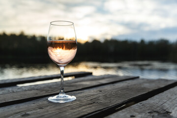 Sunset view of a glass of orange wine on a wooden pier on a lake.