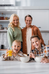 happy husband and wife standing near sons having breakfast in kitchen