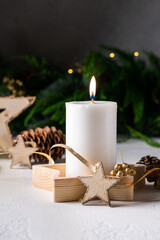 White advent candle on wooden box with christmas lights, cones, wooden star. Vertical