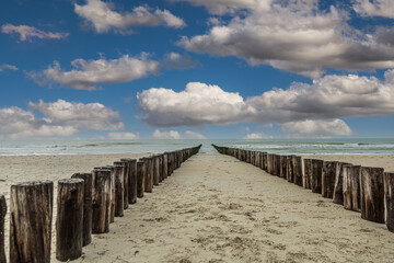 Sandy beach at Burgh-Haamstede in the Dutch province of Zeeland with a double row of posts of beach in the sea intended as functional coastal protection with veil clouds and cumulus clouds