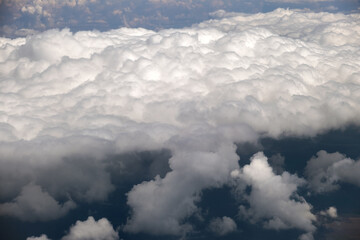 Aerial view from airplane window of white puffy clouds on bright sunny day.