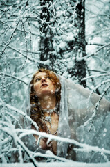 Beautiful young sexy snow girl with red hair on winter nature in a cold winter forest with Snowfall.