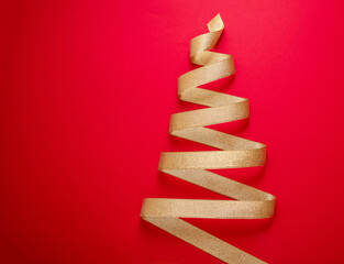Christmas tree shape golden ribbon on red color background. Gold shiny curly tape, minimal design