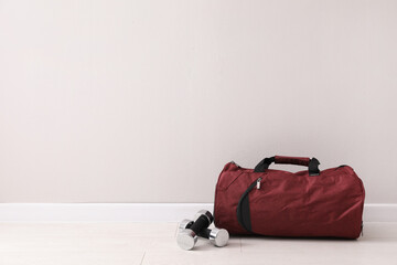Red sports bag and dumbbells on floor near light wall, space for text