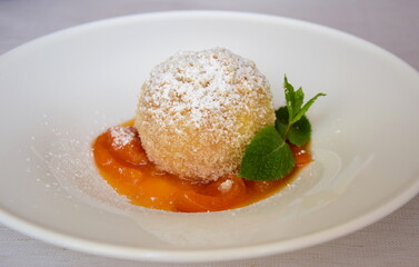 Marillenknödel mit Marillenröster, Staubzucker und Semmelbrösel auf weißen Teller. Traditionelle Nachspeise aus Südtirol und Österreich