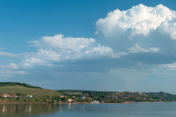 group of white cumulus clouds on blue sky over hilly river bank as natural background