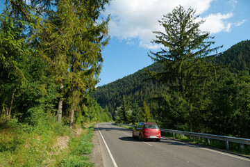 Red car drives on the beautiful road through the forest in Carpathian Mountains
