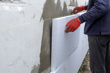 Construction worker installing styrofoam insulation sheets on house facade wall for thermal protection.