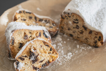 Traditional Christmas stollen made of dried fruits and nuts sprinkled with powdered sugar on the background of a Christmas decor with candles. Traditional Christmas cupcake