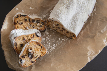 Traditional Christmas stollen made of dried fruits and nuts sprinkled with powdered sugar on the background of a Christmas decor with candles. Traditional Christmas cupcake.