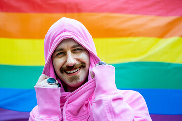 happy gay man smiling and looking at the camera, rainbow flag on background - gay pride...