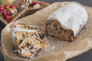 Traditional Christmas stollen made of dried fruits and nuts sprinkled with powdered sugar on the background of a Christmas decor with candles. Traditional Christmas cupcake