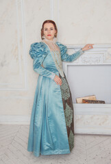 Beautiful young woman in medieval style blue dress in the room