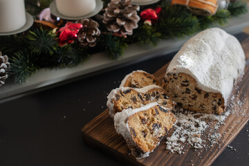 Traditional Christmas stollen made of dried fruits and nuts sprinkled with powdered sugar on the background of a Christmas decor with candles. Traditional Christmas cupcake