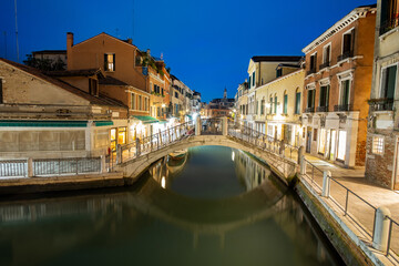 Night view of illuminated old buildings, floating boats and light reflections in canal water in Venice, Italy