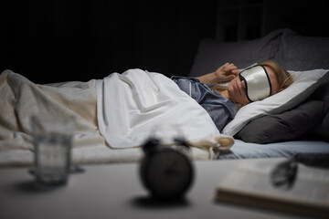 Obraz premium Relaxed mature woman in sleeping mask and pajamas having sweet dreams while lying on comfy bed with soft pillows and blanket. Concept of people and peaceful sleep.