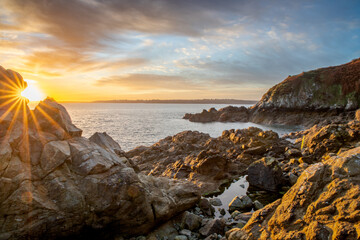 Fototapeta na wymiar lever du jour étincelant sur la mer avec un beau ciel doré et des rochers en avant-plan (Bretagne, France)
