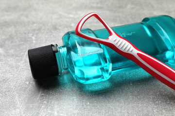 Red tongue cleaner and mouthwash on grey table, closeup