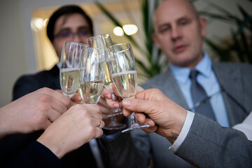 Successful business people are clinking glasses of champagne and smiling while celebrating in office