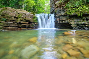 Waterfall on mountain river with white foamy water falling down from rocky formation in summer forest.