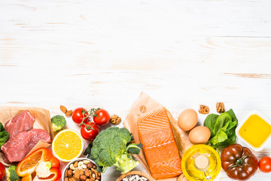 Healthy food products at white. Balanced nutrition. Salmon fish, beef, cheese, beans, nuts and vegetables with olive oil. Top view image with copy space.