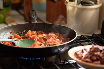 Carne en sartén con cebolla y tomate. Comida tradicional hecha en casa en un estufa por la tarde.