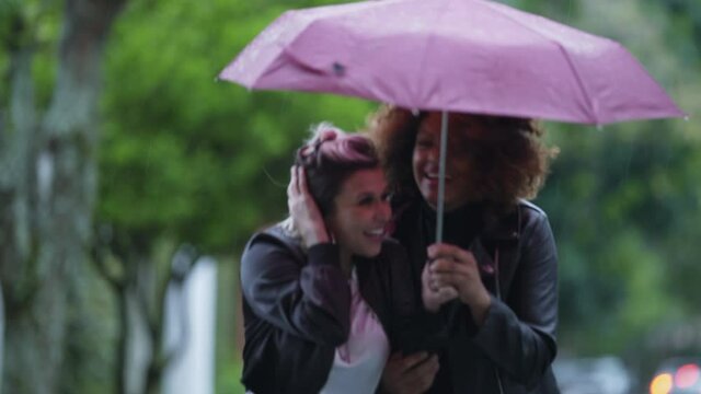 Two Brazilian women sharing umbrella during tropical rain in Brazil
