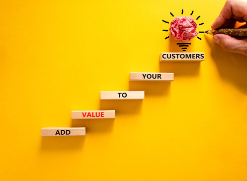 Add value to your customers symbol. Concept words 'Add value to your customers' on blocks on a yellow background, copy space. Businessman hand, light bulb icon. Business, customers value concept.