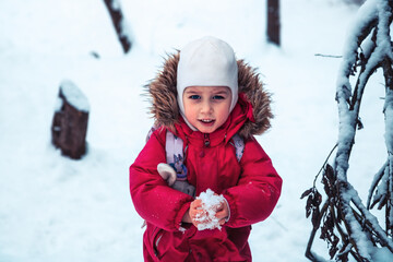 Small beautiful child girl making snowball in hands in cold winter day  