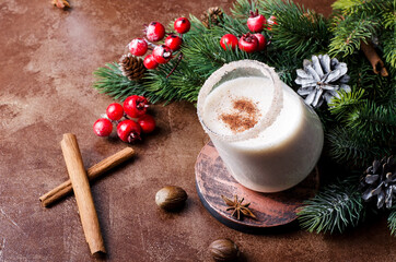 Egg punch on a brown background with Christmas tree branches and decorative decorations. Christmas drink eggnog in a glass