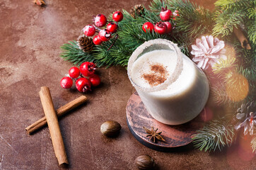 Egg punch on a brown background with Christmas tree branches and decor and bokeh. Eggnog Christmas drink in a glass glass