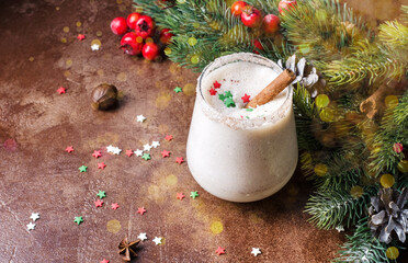 Egg punch on a brown background with Christmas tree branches and decor and bokeh. Eggnog Christmas drink in a glass glass