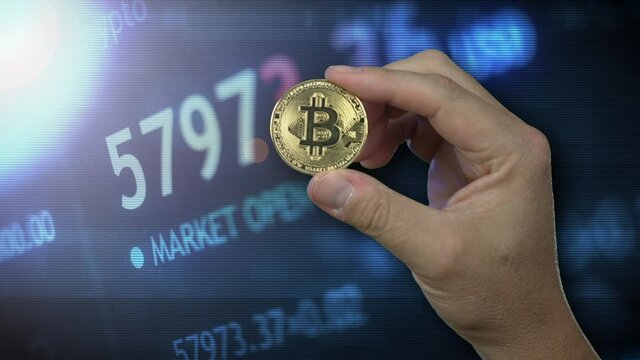 A man holds a gold Bitcoin in front of a stylized cryptocurrency market screen.  	