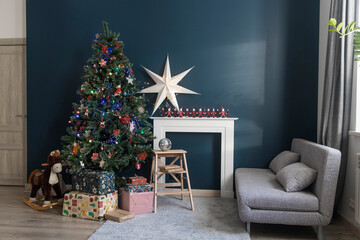 Home decoration before Christmas. Decorated Christmas tree with garland lights, rocking horse, gifts wrapped in elegant paper, artificial fireplace with a large white paper star and candles.