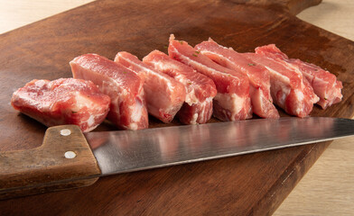 Pork rib, raw pork rib, in pieces and seasoned, with garlic, onion and rosemary on rustic wood and a knife, selective focus.