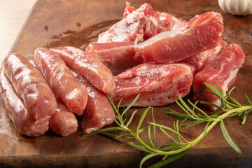 Pork rib, raw pork rib, in pieces and seasoned and sausage sections, with garlic, onion and rosemary on rustic wood and a knife, selective focus.