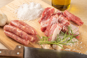 Pork ribs, sausage segments, rock salt, garlic, onion, rosemary and olive oil on a light rustic...