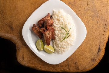 Fried pork ribs, rice and condiments on a white plate arranged on light rustic wood, selective focus.