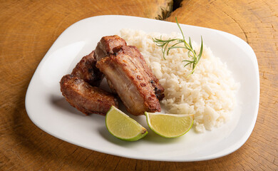 Fried pork ribs, rice and condiments on a white plate arranged on light rustic wood, selective focus.