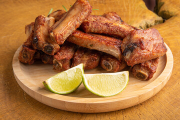 Fried pork ribs with lemon and spices on wood laid out on light rustic wood, selective focus.