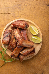 Fried pork ribs with lemon and spices on wood laid out on light rustic wood, selective focus.