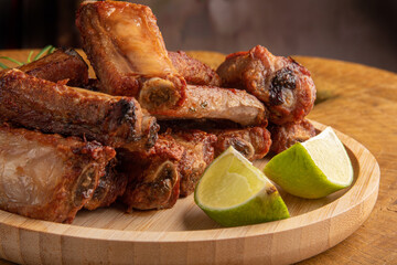 Fried pork ribs with lemon and spices on wood laid out on light rustic wood, selective focus.