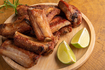 Fried pork ribs with lemon and spices on wood laid out on light rustic wood, selective focus.