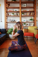 Side view of a fit woman sitting on a yoga mat at home in the lotus position and meditating.