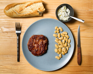 Tasty grilled burger served with coocked vegetarian beans in a plate on a rustic wooden table. Flat lay, top view