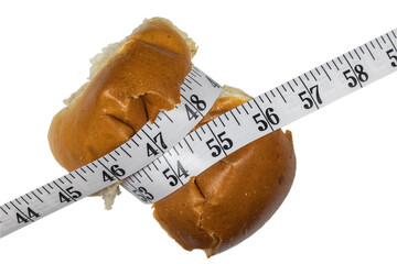 Bun compressed with measuring tape. The concept of willpower when losing weight. Weight and diet control. Bun on white background.