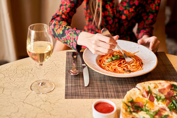 Woman eats Italian pasta with tomato, meat. Close-up spaghetti Bolognese wind it around a fork with...