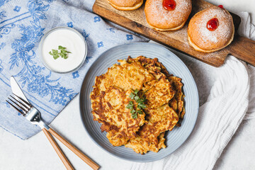 Traditional Jewish festive food for Hanukkah holiday. Jew festival of lights. Potato pancakes Latkes and Sufganiyot jelly doughnuts cooked in oil on white table. Flat lay, top view.