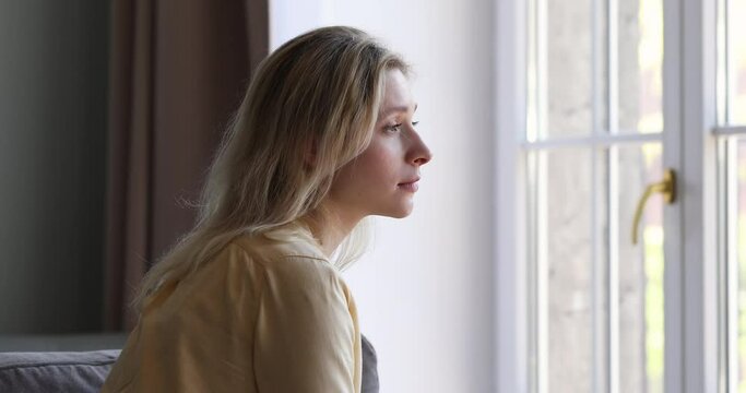 Profile of sad nervous pretty woman sit on sofa alone look at window suffer from solitude divorce heartbreak love life problem. Depressed upset young lady lost in bad thoughts need psychological help
