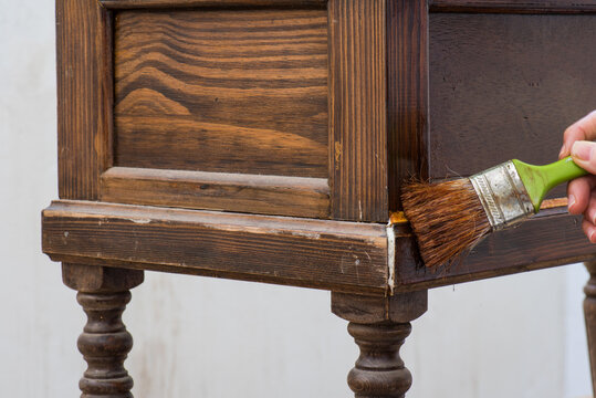 Con un pincel en la mano, barnizando un mueble de madera antiguo
